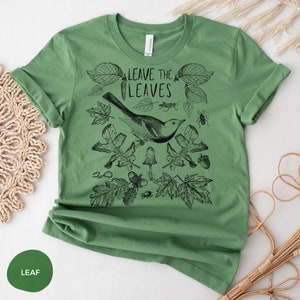May include: Green t-shirt with a black and white illustration of a bird, leaves, and other nature elements. The text "Leave the Leaves" is printed on the shirt.