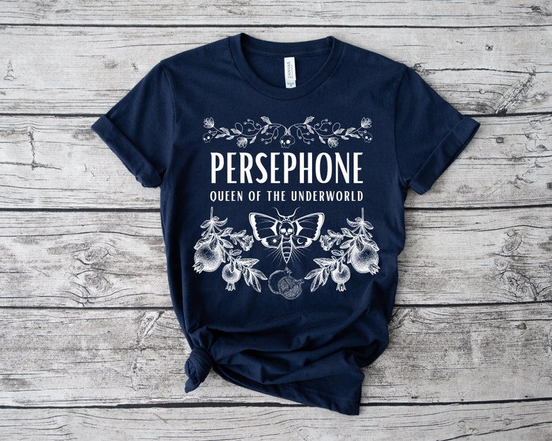 May include: A navy blue t-shirt with a white graphic design featuring the text "PERSEPHONE QUEEN OF THE UNDERWORLD" with a stylized moth and pomegranate imagery.