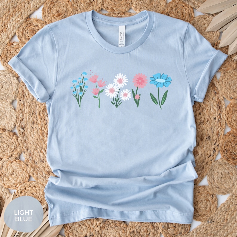 May include: Light blue t-shirt with a row of colorful flowers printed on the front. The flowers are pink, white, and blue.