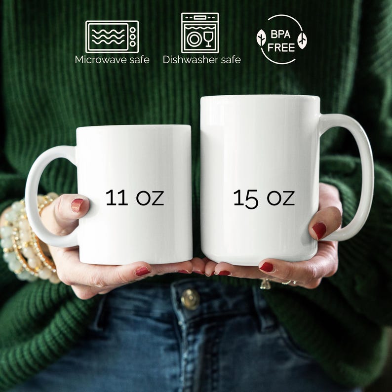 K&ouml;nnte beinhalten: Zwei wei&szlig;e Keramikbecher, einer mit der Aufschrift "11 oz" und der andere mit "15 oz", werden vor einem gr&uuml;nen Pullover und einer blauen Jeans gehalten. Die Becher haben gebogene Griffe. Symbole zeigen, dass sie mikrowellen- und sp&uuml;lmaschinenfest und BPA-frei sind.