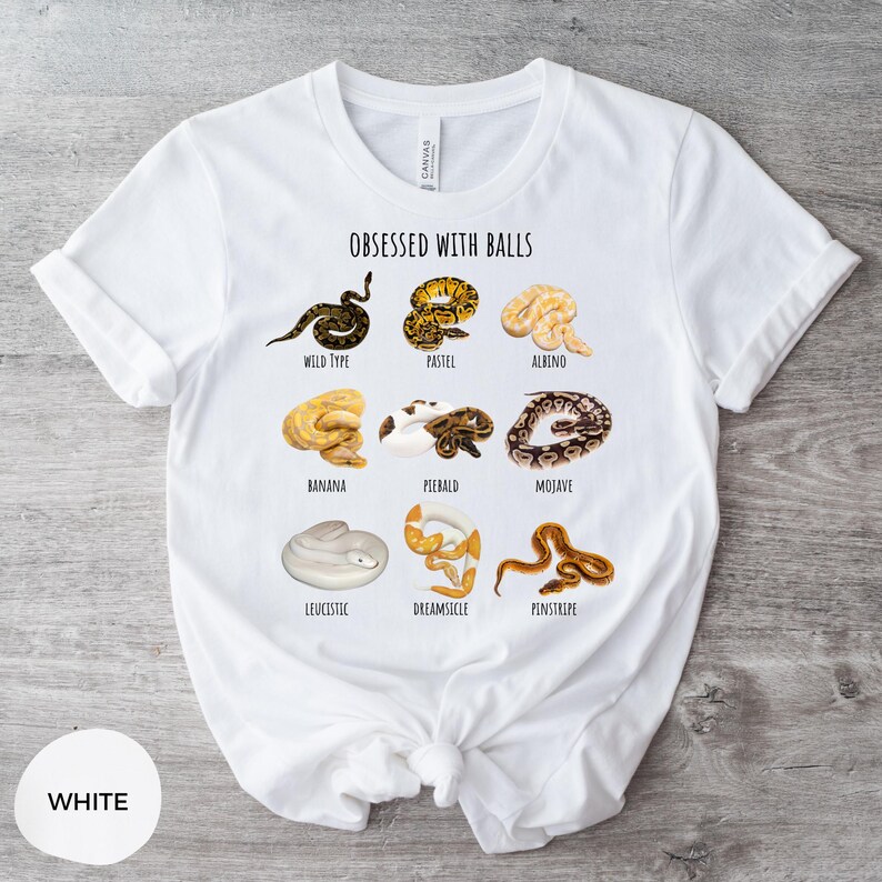 May include: White t-shirt with the text "OBSESSED WITH BALLS" and illustrations of various snake morphs, including Wild Type, Pastel, Albino, Banana, Piebald, Mojave, Leucistic, Dreamsicle, and Penstripe. The shirt is made of a soft material.