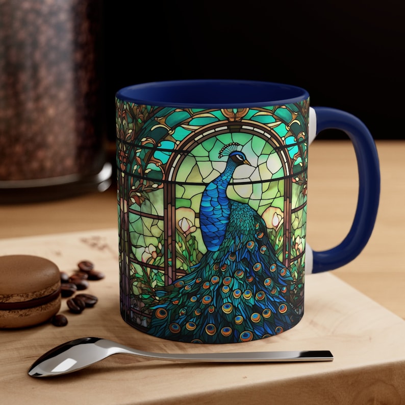 May include: A blue and green ceramic coffee mug with a stained glass design of a peacock. The mug has a dark blue rim and handle.