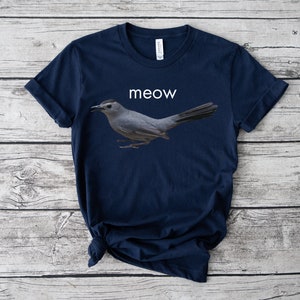 May include: A navy blue t-shirt with a gray bird graphic and the word "meow" printed in white.