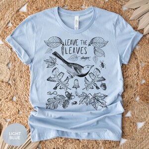 May include: Light blue t-shirt with a black and white illustration of a bird, leaves, and insects. The text "Leave the Leaves" is printed on the shirt.