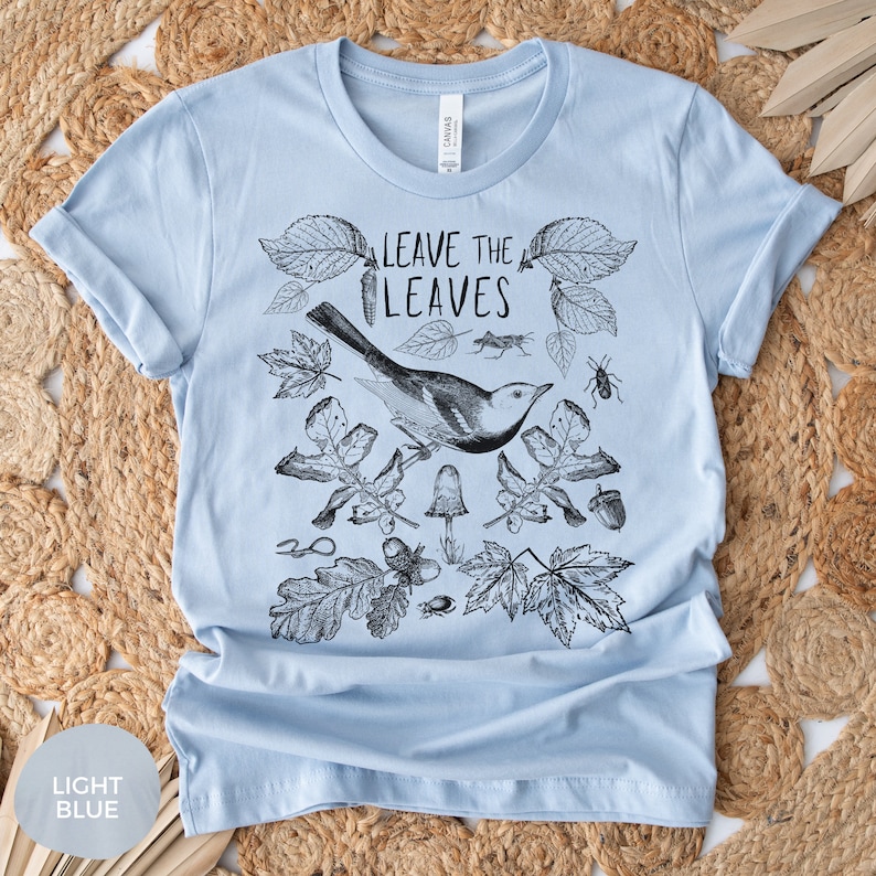 May include: Light blue t-shirt with a black and white illustration of a bird, leaves, and insects. The text "Leave the Leaves" is printed on the shirt.