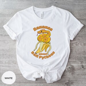 Op de afbeelding: Wit T-shirt met een afbeelding van een gele banaan met een ball python eromheen gewikkeld. De tekst "Bananas about Ball Pythons" staat op het shirt gedrukt.
