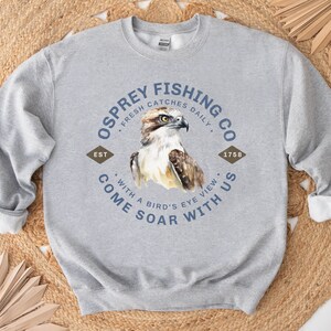 May include: Gray sweatshirt with a blue and white logo that says "Osprey Fishing Co. Fresh Catches Daily. Est 1758. Come Soar With Us. With a Bird's Eye View."