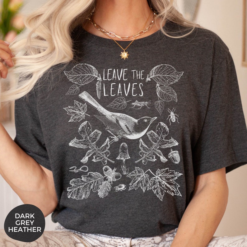 May include: A dark heather grey t-shirt with a white graphic design featuring a bird, leaves, and the text "Leave the Leaves".
