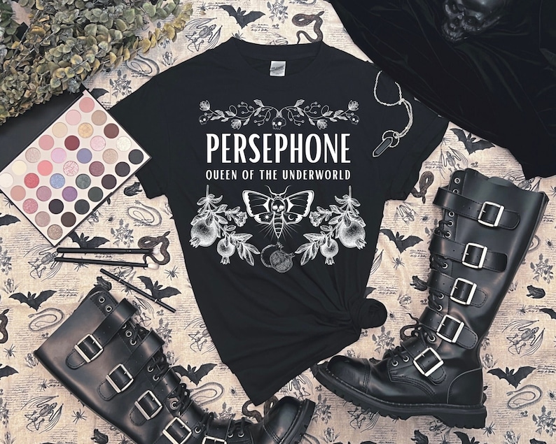 May include: Black t-shirt with white graphic print of a moth and floral design. The text "PERSEPHONE QUEEN OF THE UNDERWORLD" is printed on the shirt.