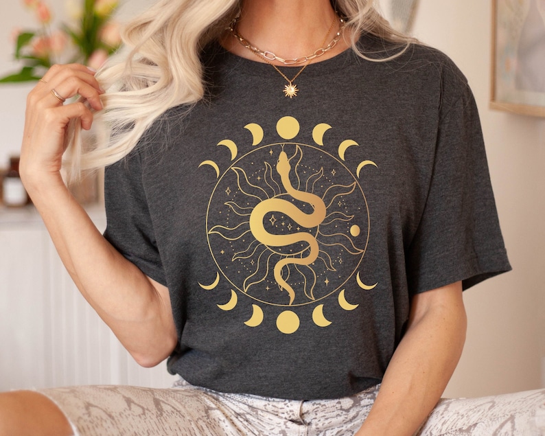 May include: A dark gray t-shirt with a gold graphic of a snake wrapped around a sun with a crescent moon design.