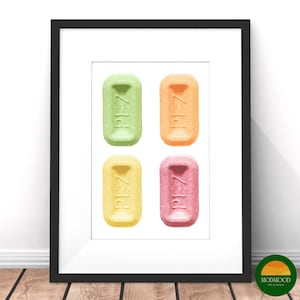 Może przedstawiać: Oprawiony wydruk przedstawiający cztery kolorowe cukierki PEZ w kolorach zielonym, pomarańczowym, żółtym i różowym. Na każdym cukierku znajduje się napis "PEZ". Wydruk jest na białym tle i oprawiony w czarną ramę.