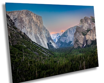 May include: A panoramic view of a valley in Yosemite National Park, California. The valley is surrounded by towering granite cliffs, with a waterfall cascading down one of the cliffs. The sky is a vibrant blue, with a hint of orange in the distance.