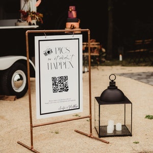 Könnte beinhalten: Ein weißes Schild mit schwarzem Text, der "Pics or it didn't happen" lautet, mit einem QR-Code und dem Text "Bitte teilen Sie Ihre Fotos mit uns! Scannen Sie einfach mit Ihrem Smartphone und laden Sie sie hoch." Das Schild steht auf einem Kupferständer und im Vordergrund befindet sich eine schwarze Laterne mit Kerzen.