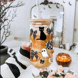 May include: A clear glass tumbler with a black cat, pumpkins, and bows printed on it. The tumbler has a bamboo lid and two clear straws. The text "Trick or Treat" is printed on the tumbler.