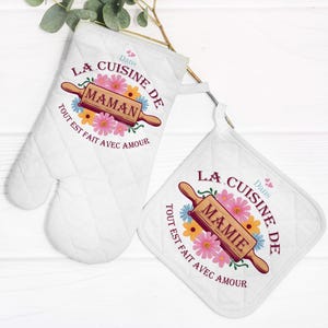 Peut inclure: Deux maniques de cuisine blanches avec des motifs floraux et le texte "Dans la cuisine de Maman" et "Dans la cuisine de Mamie". Les maniques sont en tissu matelassé et ont une boucle de suspension.