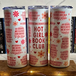 Peut inclure: Trois gobelets isothermes blancs avec couvercles, décorés de motifs floraux et de texte. L'un des gobelets indique "HOT GIRL BOOK CLUB" en rouge. Les deux autres présentent des citations et des phrases liées aux livres en rouge. Les gobelets sont posés sur un plateau en bois.