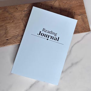 May include: A light blue reading journal with the text "Reading Journal" in black lettering and a small heart symbol.