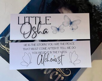 May include: Two white bookmark designs with black text and butterfly illustrations. The top bookmark says "LITTLE Osha" with three blue butterflies. The bottom bookmark says "HE IS THE STORM. YOU ARE THE PEACE THAT MUST COME AFTER IT. TELL ME DO YOU BELIEVE IN THE FATES Alchemist"