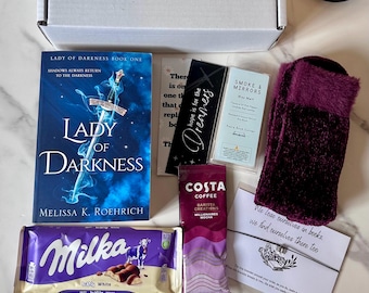 May include: A gift box containing a book, chocolate, coffee, bookmarks, and socks. The book is titled "Lady of Darkness." The chocolate is Milka, and the coffee is Costa. The socks are a deep purple colour. The box is on a white surface.