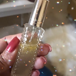 Puede incluir: Una botella de vidrio transparente con una tapa plateada, llena de un líquido amarillo claro. La botella tiene un diseño texturizado y se sostiene en una mano.