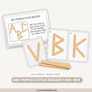 May include: An educational activity set featuring a clear plastic box with a label reading ABC POPSICLE STICK BUILDER, accompanied by white cards displaying letters V, B, and K formed with light brown wooden sticks, plus two loose sticks.