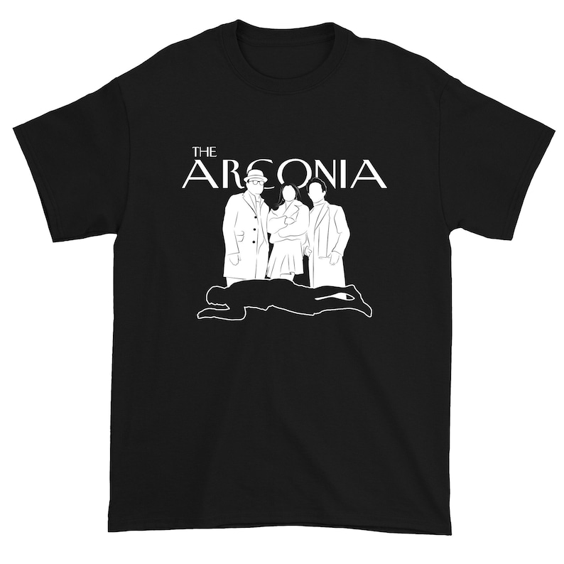 Puede incluir: Camiseta negra con un gr&aacute;fico blanco de tres figuras de pie frente a una figura ca&iacute;da. El texto "THE ARCONIA" est&aacute; por encima de las figuras.