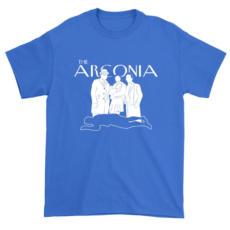 Puede incluir: Una camiseta azul real con un gr&aacute;fico blanco de una familia de cuatro personas de pie frente a la silueta de una persona tendida en el suelo. El texto "THE ARGONIA" est&aacute; por encima de la familia.