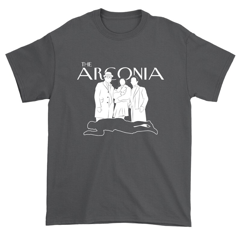 Puede incluir: Una camiseta gris oscuro con un dise&ntilde;o gr&aacute;fico blanco que presenta el texto "THE ARCONIA" y una silueta de tres personas.