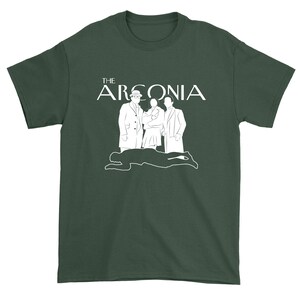 Puede incluir: Una camiseta verde oscuro con un gr&aacute;fico blanco de tres personas de pie frente al texto "THE ARCONIA".