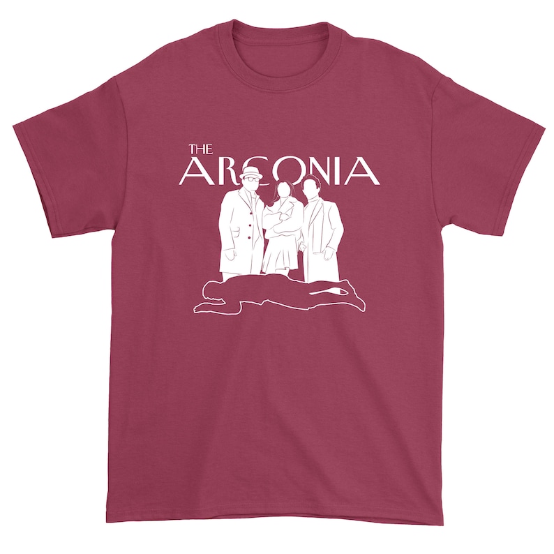 Puede incluir: Una camiseta de color granate con un gr&aacute;fico blanco de tres figuras de pie frente a la silueta de una persona tendida en el suelo. El texto "THE ARCONIA" est&aacute; por encima de las figuras.