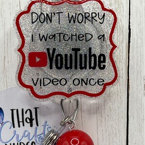 May include: A badge reel with a glittery silver and red scalloped edge. The badge reads "DON'T WORRY I WATCHED A YouTube VIDEO ONCE" with the YouTube logo. A red ball and a clear plastic piece are attached.