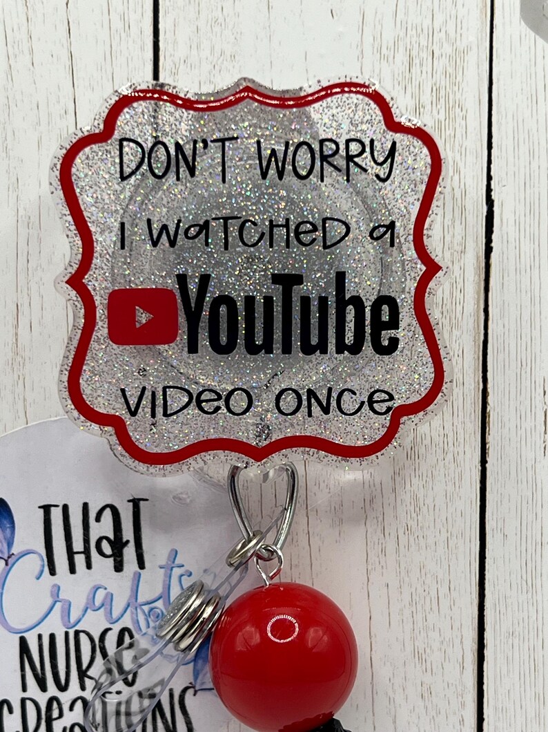 May include: A badge reel with a glittery silver and red scalloped edge. The badge reads "DON'T WORRY I WATCHED A YouTube VIDEO ONCE" with the YouTube logo. A red ball and a clear plastic piece are attached.