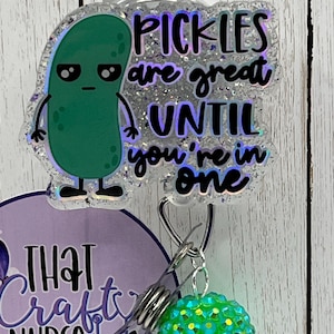 May include: A badge reel with a green pickle cartoon and the text "PICKLES are great UNTIL you're in one." The badge reel has a clear plastic clip and a green and blue rhinestone charm.