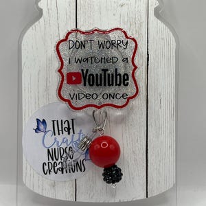 May include: A clear acrylic badge reel with a red and black beaded charm. The badge reel has the text "DON'T WORRY I WATCHED A YOUTUBE VIDEO ONCE". A smaller circle has the text "THAT Nurse CREATIONS".