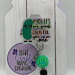 May include: A badge reel with a green pickle cartoon and the text "Pickles are great until you're in one." The reel has a green and black charm and a purple logo that says "That Crafts Nurse Creations."