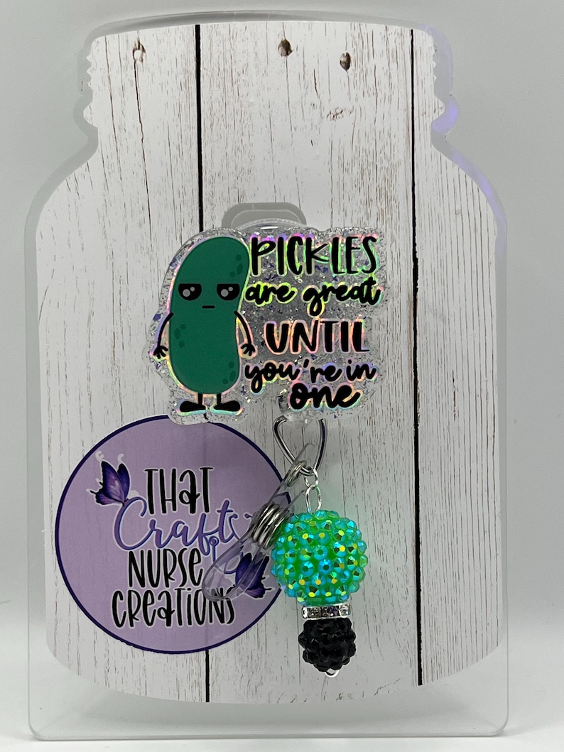 May include: A badge reel with a green pickle cartoon and the text "Pickles are great until you're in one." The reel has a green and black charm and a purple logo that says "That Crafts Nurse Creations."