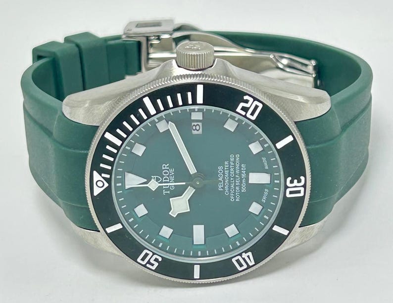 May include: A stainless steel Tudor Pelagos watch with a green dial and bezel. The watch has a green rubber strap and a date window at the 3 o'clock position. The watch is water resistant to 500m.