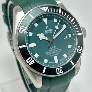 May include: A green Tudor Pelagos watch with a black and white bezel. The watch has a green dial with white markers and hands. The watch band is green. The watch is water resistant to 1640 feet.