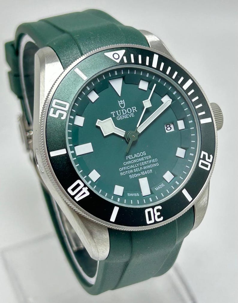 May include: A green Tudor Pelagos watch with a black and white bezel. The watch has a green dial with white markers and hands. The watch band is green. The watch is water resistant to 1640 feet.