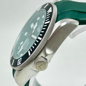 May include: A silver-toned wristwatch with a black and white bezel and a green watch band. The watch face is a light green color. The bezel has the number "02" on it.