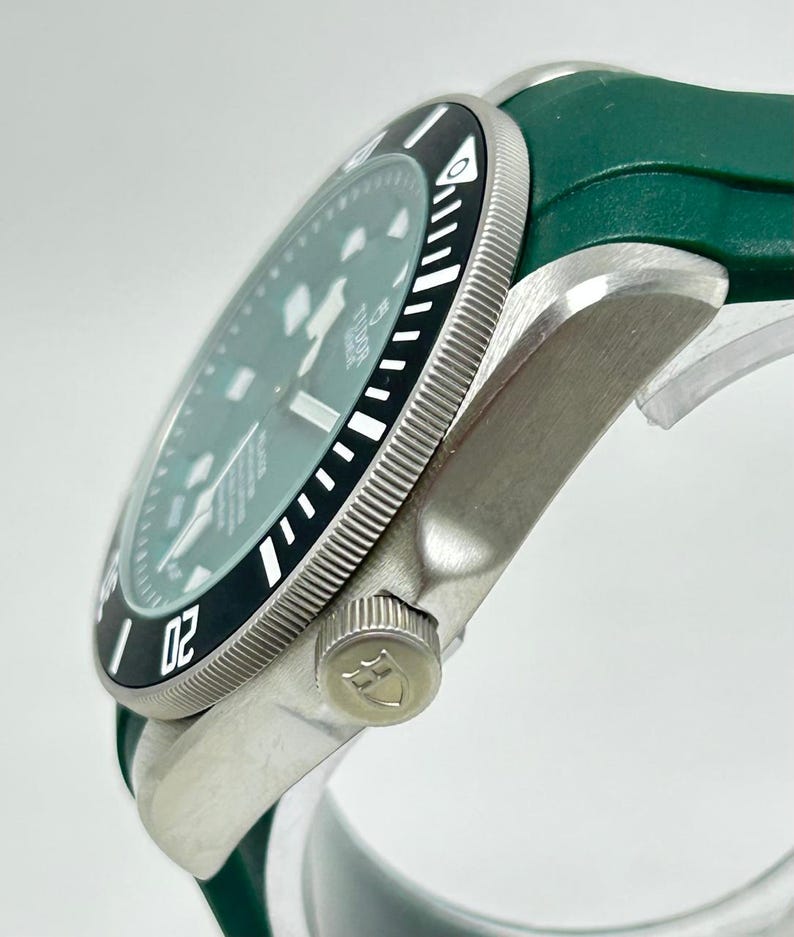 May include: A silver-toned wristwatch with a black and white bezel and a green watch band. The watch face is a light green color. The bezel has the number "02" on it.