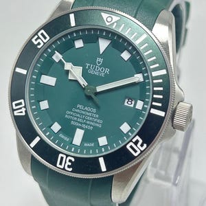 May include: A green and silver wristwatch with a black bezel. The watch face displays the brand name "TUDOR GENEVE" and the model "PELAGOS". The watch has a green rubber strap and is water resistant to 1640 feet.