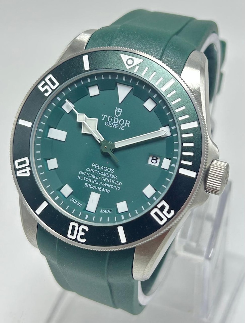 May include: A green and silver wristwatch with a black bezel. The watch face displays the brand name "TUDOR GENEVE" and the model "PELAGOS". The watch has a green rubber strap and is water resistant to 1640 feet.