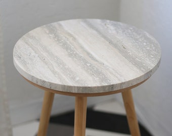 May include: A round, white marble top side table with a wood base and three legs. The table is sitting on a black and white tiled floor.