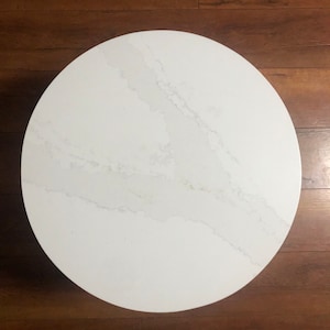 May include: A white round table top with a grey veined pattern. The table top is made of a smooth, polished material.