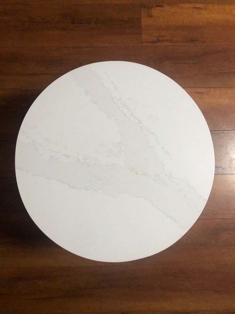 May include: A white round table top with a grey veined pattern. The table top is made of a smooth, polished material.