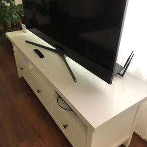 May include: White entertainment center with three drawers and a shelf. A black television is sitting on top of the entertainment center.