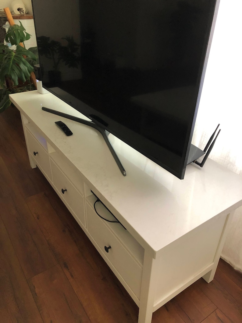 May include: White entertainment center with three drawers and a shelf. A black television is sitting on top of the entertainment center.