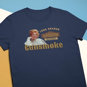 May include: A navy blue t-shirt with a vintage-style graphic of a saloon with the text "Long Branch Saloon" and "Miss Kitty Russell, Owner-Operator" and the word "Gunsmoke" underneath.
