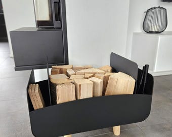May include: Black metal log holder with wooden legs, filled with stacked firewood. The holder is next to a black fireplace.